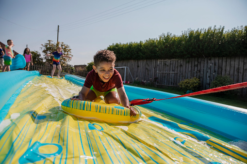 Children playing outside in a garden in the North East of England on a slip and slide. They are laughing and having fun and a boy is being pulled down the slide.