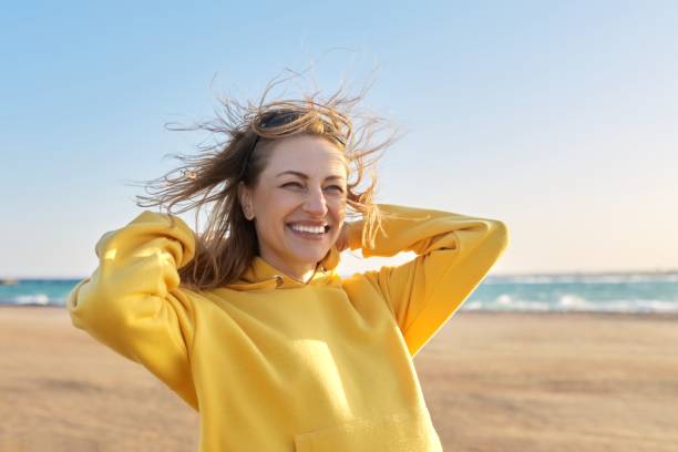 Outdoor portrait of smiling happy blonde woman 45 years old looking at camera Outdoor portrait of smiling happy blonde woman 45 years old looking at camera. Sunny day on sea coast, beach blue sky background 40 49 years stock pictures, royalty-free photos & images