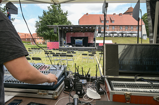 Analog and digital mixing consoles, receivers for wireless microphones and the hand of the sound mixer at the soundcheck for an open air festival, selected focus, narrow depth of field