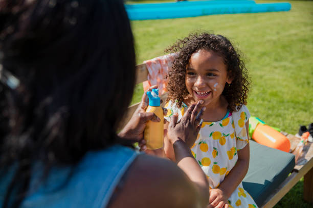 Mummy Protecting me from the Sun Over the shoulder view of a mother putting suncream on her daughter. They are in a garden in the North East of England in summer. suntan lotion stock pictures, royalty-free photos & images