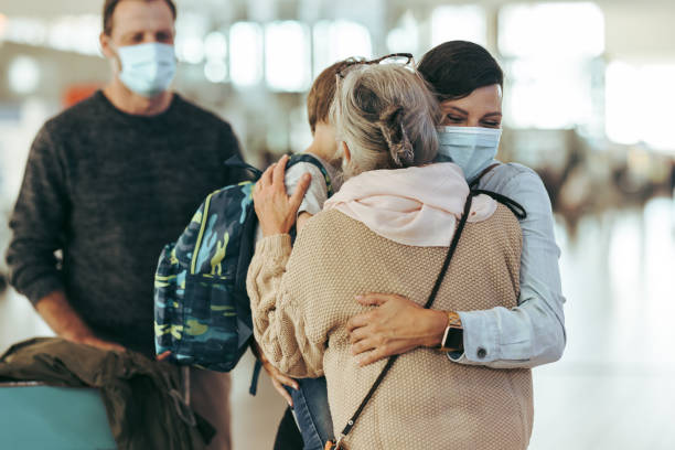 Grandma welcoming family arriving after pandemic at airport Mother embracing her daughter and grandson at airport arrival gate. Woman with her son giving hug to her mother at airport in pandemic. airport hug stock pictures, royalty-free photos & images