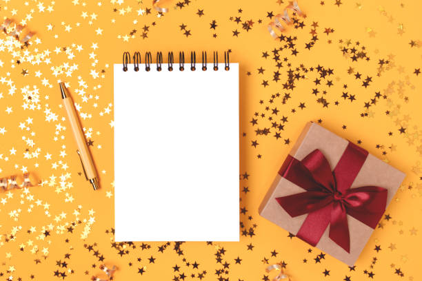 istock Blank notebook mockup, gift box with red ribbon and gold stars confetti. 1334436078