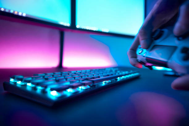 istock Close-up of player hands holding game controller. Gaming accessories and pink illuminated wall in background. 1334436144