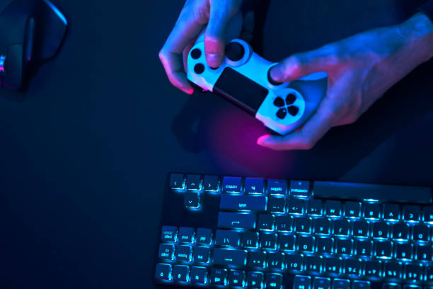 istock Top down view of controlling devices. Backlit computer keyboard, mouse and hands holding game controller. 1334436856