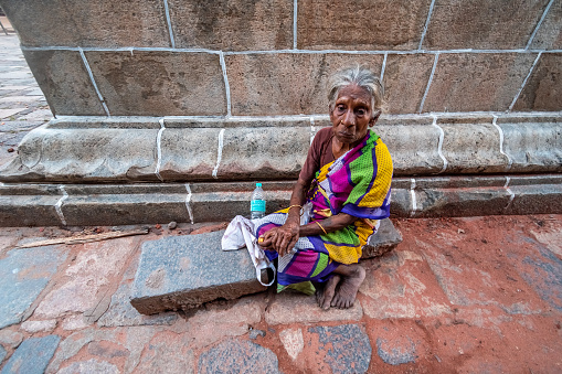 Chidambaram, Tamil Nadu, India - February 2020: An elderly Indian woman sitting on a stone platform outside the walls of a shrine in the ancient Nataraja temple.