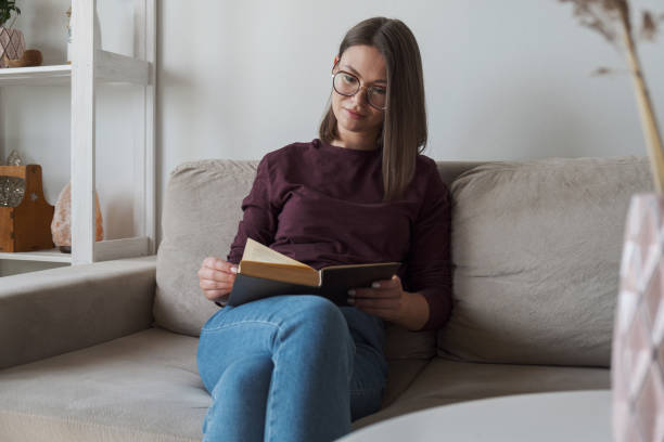 istock Woman reading book sitting in sofa at home 1334438731