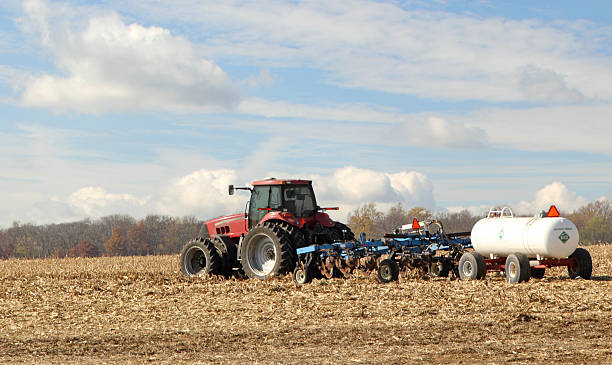 Plowing and Fertilizing Farm Field Red tractor pulling plow and anhydrous ammonia tank ammonia fertilizer stock pictures, royalty-free photos & images
