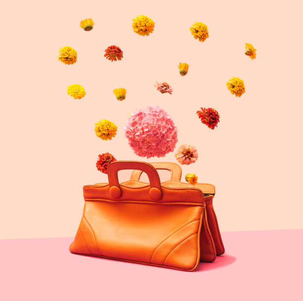 Levitation concept. Various head summer flowers flying, falling and levitating over a very old natural color leather female handbag. Minimalist arrangement against light and dark pink background.