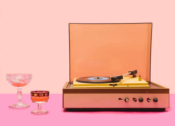 istock Gramophone record player from sixties. Turntable for single vinyl with pink bottom with light pink background. Two cocktail glasses, party vibe. 1334443807