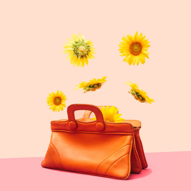 istock Levitation concept. Sunflower head flowers flying, falling and levitating over a very old natural color leather female handbag. Minimalist arrangement against light and dark pink background. 1334444408