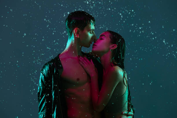 pareja joven, hombre y mujer abrazándose, besándose bajo la lluvia sobre fondo azul a luz de neón. - blowing men kissing blowing a kiss fotografías e imágenes de stock