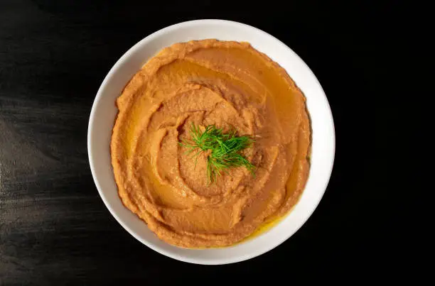 Photo of Famous traditional Arabic cuisine - peeled fava beans mashed plain in a white bowl on dark brown background. Top view. Foul Mudammas