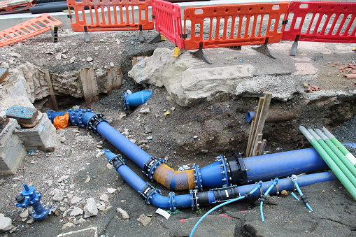 Blue gas and water canalisation pipes showing on a hole in the ground and tarmac at a roadworks site in Edinburgh Scotland