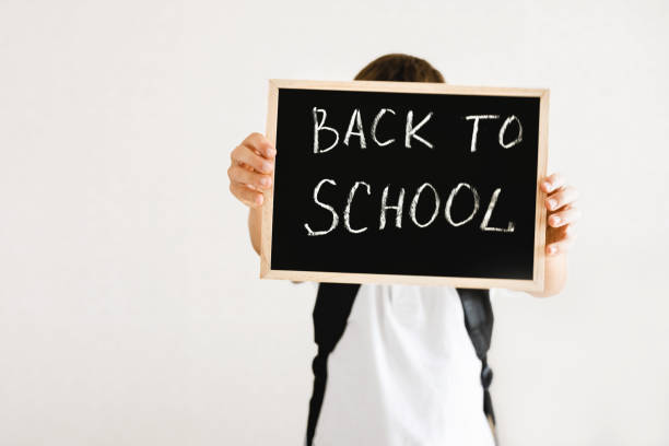 istock Boy with backpack holding in his hands chalk board with inscription Back to school isolated on white background 1334459948