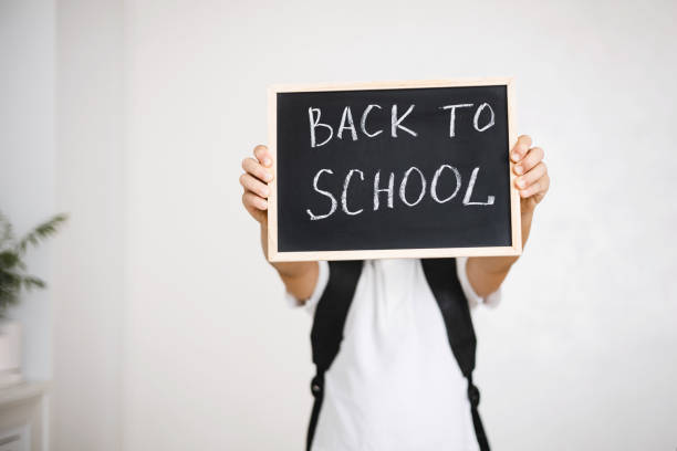 istock Boy with backpack holding in his hands chalk board with inscription Back to school isolated on white background 1334459954