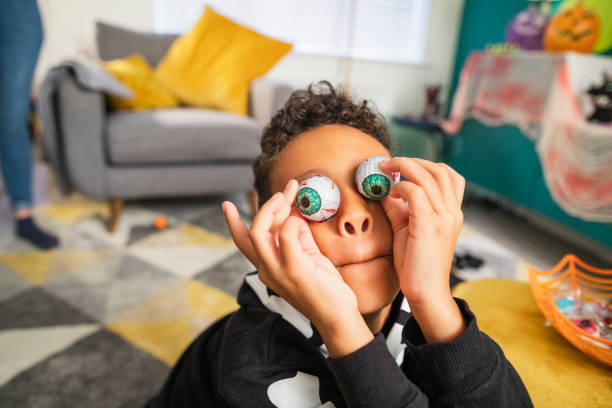 Spooky Halloween Treats A front-view close-up shot of a young boy wearing a skeleton costume for Halloween. He is smiling and looking at the camera while holding spooky eyeball chocolate balls over his eyes. eye candy stock pictures, royalty-free photos & images