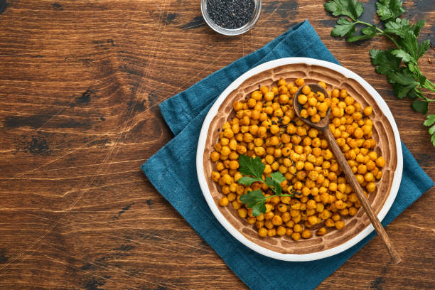 istock Fried chickpeas with turmeric in ceramic plate on an old wooden table background. Roasted spicy chickpeas or Indian chana or chole, popular snack recipe. Top view. 1334462844