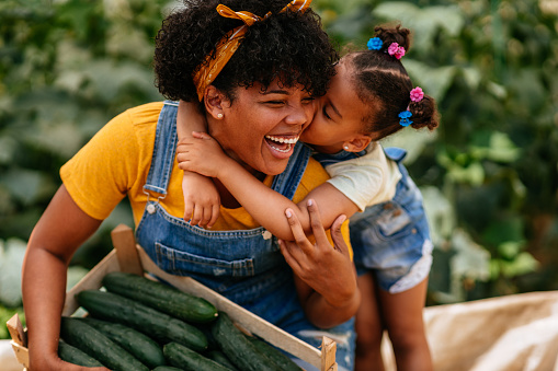 Adorable little girl hugging her mother during cucumber harvest in greenhouse