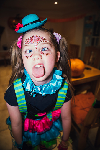 A Close up of a young girl with her hair in bunches and her tongue sticking out as she makes a funny face to the camera at a family Halloween party in the North East of England.