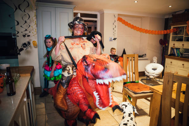 Funny Halloween Costume A front view of a young woman showing her funny side in her choice of inflatable Halloween costume which is her riding on the back of a dinosaur. You can also see different family members also in costume as they enjoy themselves at the family Halloween party! party funny stock pictures, royalty-free photos & images