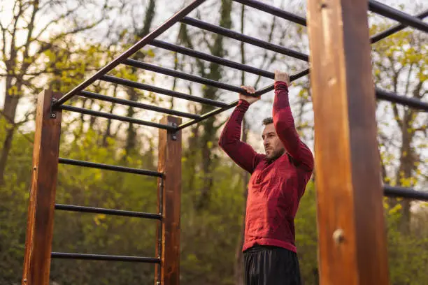 Men in sportswear doing pull ups while working out outdoors in a street workout park