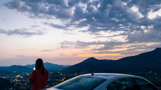 Young woman standing on the top of the hill and taking photo of cityscape via cellphone