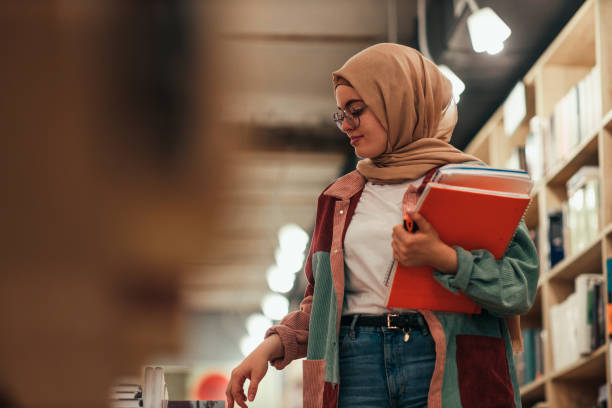 istock Islamic student at library holding books 1334469206