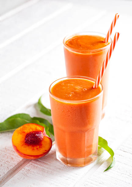 Two fresh yellow peach smoothies on a bright wooden surface with copy space