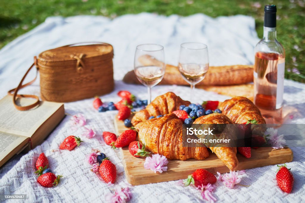 Beautiful picnic with rose wine, French croissants and fresh berries Beautiful picnic with rose wine, French croissants and fresh berries served for two on the grass covered with pink fallen petals and flowers Rosé Wine Stock Photo