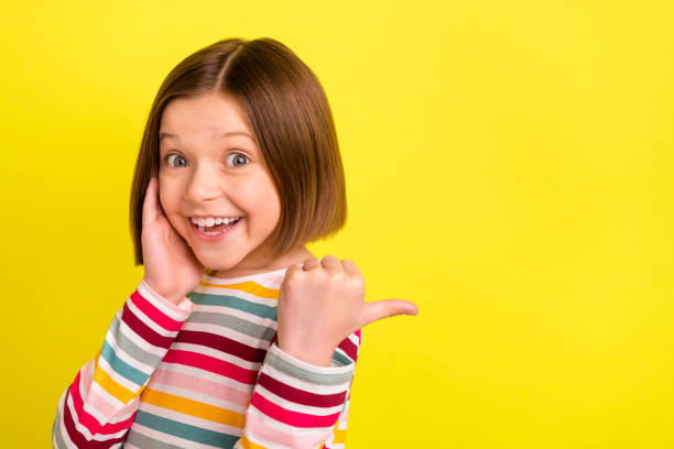 photo portrait little girl touching cheek pointing copyspace thumb smiling happy isolated bright yellow color background - surprise child little girls shock imagens e fotografias de stock