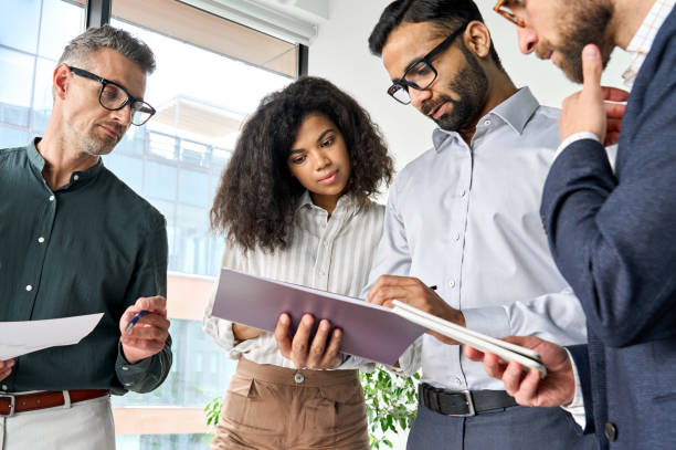 istock Diverse executive team people discussing project report standing in boardroom. 1334472979
