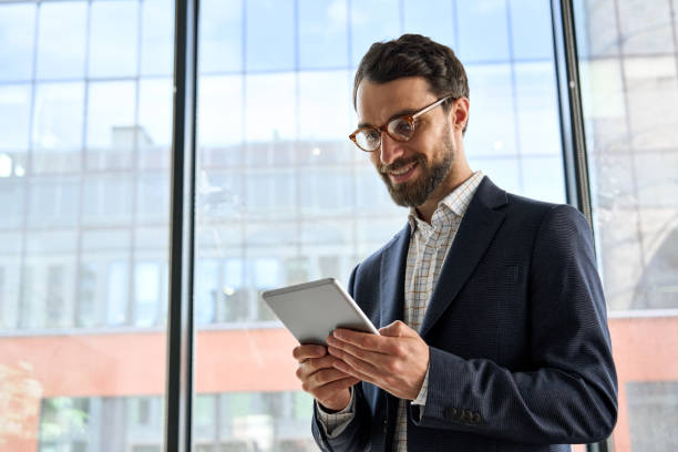 istock Smiling mature bearded businessman holding tablet device standing in office. 1334472980