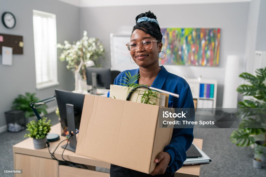 Stylish businesswoman wearing elegant blue clothes and glasses is promoted to managerial position changes office, leaves company, carries carton with packed accessories, change of job Quitting a Job Stock Photo