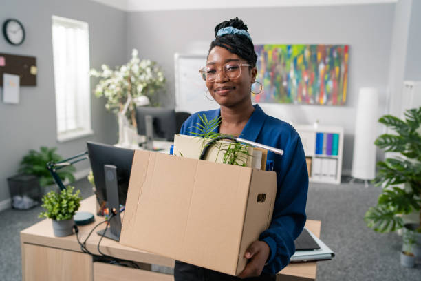 stylish businesswoman wearing elegant blue clothes and glasses is promoted to managerial position changes office, leaves company, carries carton with packed accessories, change of job - downsizing imagens e fotografias de stock