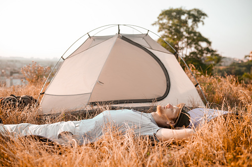 Relaxing. A man laying on the grass near his tent and looking relaxed