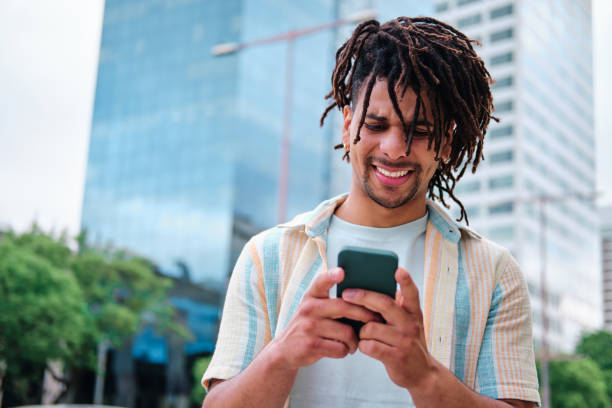 istock young man with curly hair using smartphone surrounded by modern city buildings 1334476503
