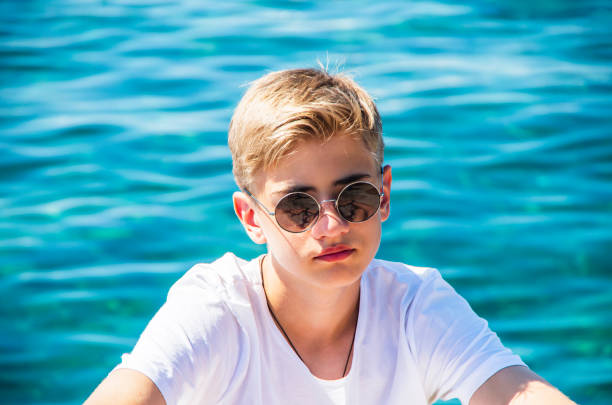 bel adolescente di 15-18 anni con occhiali da sole appoggiati sulla spiaggia. primo tempo ritratto emotivo del giovane caucasico - teenager 14 15 years 13 14 years cheerful foto e immagini stock