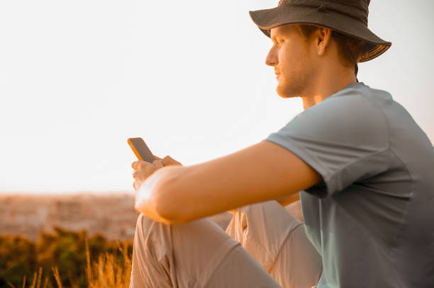 istock A man in a hat sitting on the hill and making a panoramic video 1334477054
