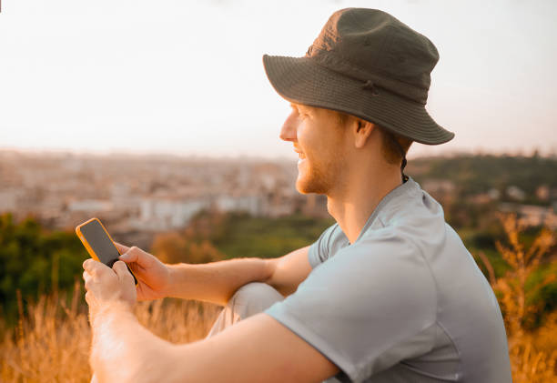 istock A man in a hat sitting on the hill and making a panoramic video 1334477072