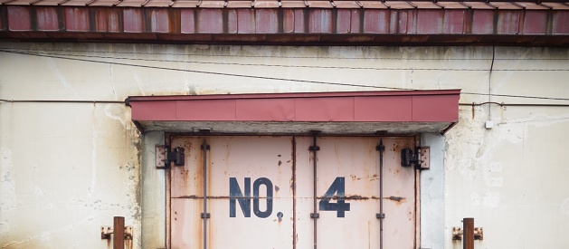 Old factory warehouse with discolored roof and number 4 on rusty door
