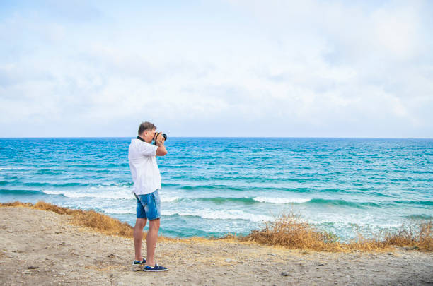 istock Middle-aged man using a DSLR camera.  Man is a professional photographer with photo camera shore enjoying  the sea, photographs the seascape 1334478904