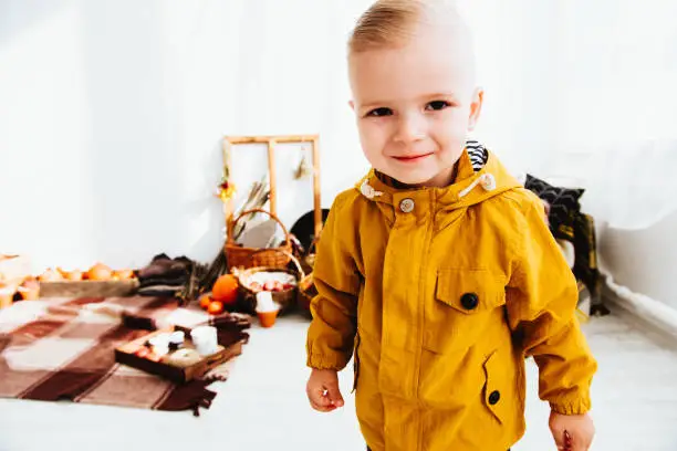 Photo of Cool trendy hipster boy 2 years old wears yellow jacket posing at the decorated photozone of autumn decor with beautiful bright autumn leaves.