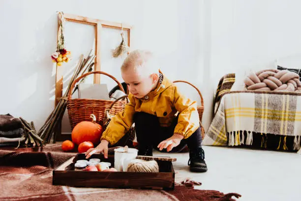 Photo of Cool trendy hipster boy 2 years old wears yellow jacket posing at the decorated photozone of autumn decor with beautiful bright autumn leaves.