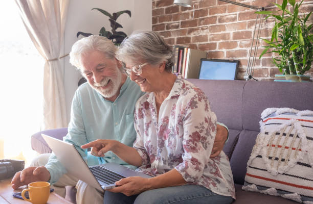 istock Carefree senior couple using laptop computer at home, sitting on sofa. Brick wall on background 1334480093