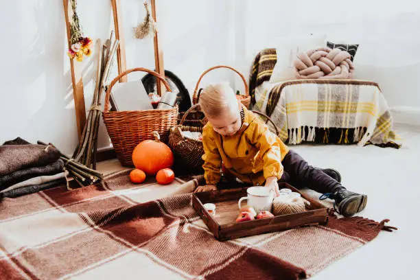 Photo of Cool trendy hipster boy 2 years old wears yellow jacket posing at the decorated photozone of autumn decor with beautiful bright autumn leaves.