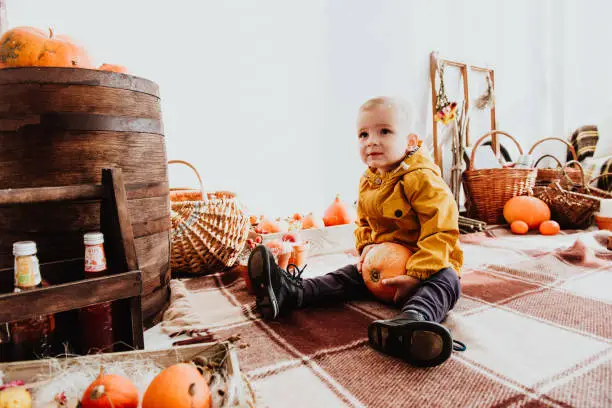 Photo of Cool trendy hipster boy 2 years old wears black posing at the decorated photozone of autumn decor with beautiful bright autumn leaves, pumpkin, apples.