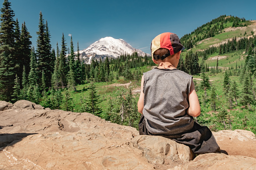 Young boy sitting on the Naches Peak Loop Trail with Mt Rainier in the background.