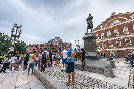Boston, MA, United States - August 9, 2021: Group of tourists and locals enjoying a street performance near the Samuel Adams Statue at Faneuil Hall in Boston, MA. Samuel Adams was an American statesman, political philosopher, and one of the founding fathers of the United States.