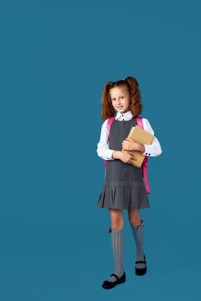 istock cute schoolgirl with backpack and book full length. 1334488557