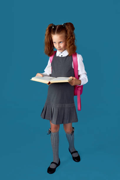 istock cute schoolgirl with backpack and book full length. 1334488591